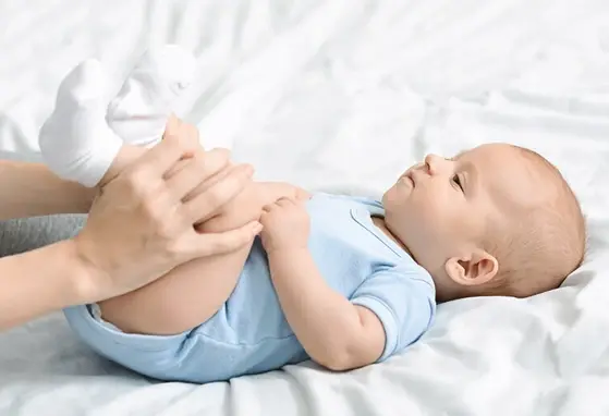 Zaparcia u niemowlaka dziecko leżące na łóżku z podkulonymi przez opiekuna nóżkami