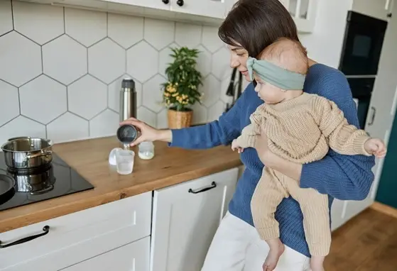Zmiana mleka modyfikowanego w diecie niemowląt – co warto wiedzieć? Mama trzymająca dziecko na rękach i przygotowująca mleko modyfikowane