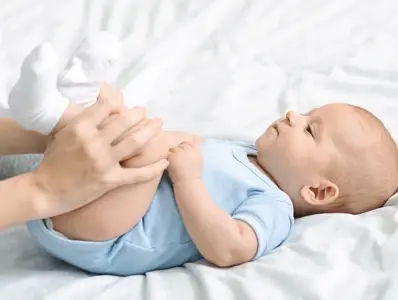 Zaparcia u niemowlaka dziecko leżące na łóżku z podkulonymi przez opiekuna nóżkami